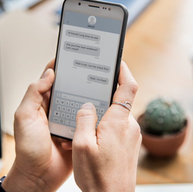 Person typing a text message on a smartphone with a small potted plant in the background.
