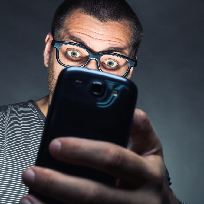 Man with glasses looking surprised while using a smartphone.