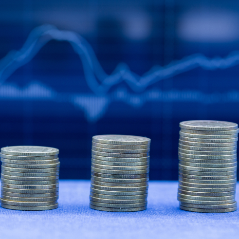 Three stacks of coins increasing in height from left to right against a backdrop with a financial graph.