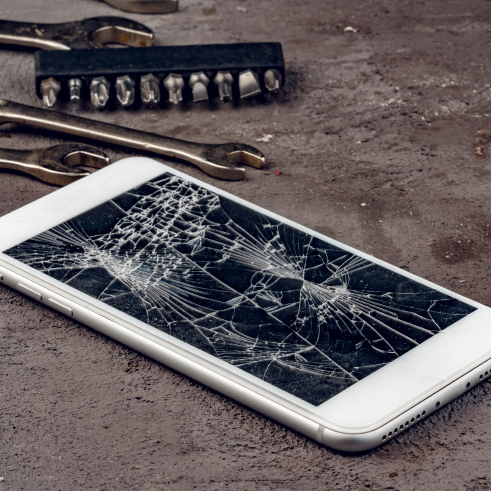 Un smartphone endommagé avec un écran brisé posé sur une surface à côté des outils.