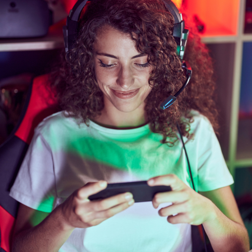 Woman with headphones using a smartphone, with colorful ambient lighting.