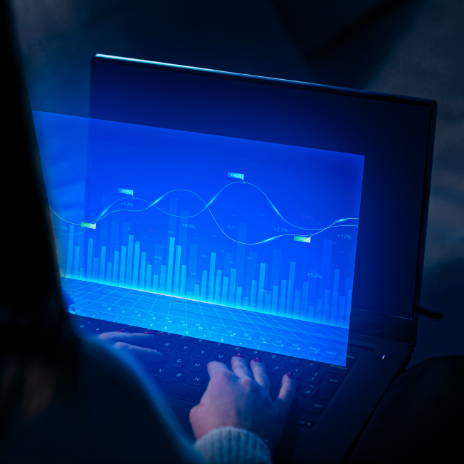 A person analyzing financial graphs on a laptop screen in a low-light environment.