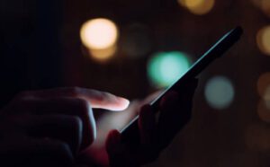 A person interacts with a smartphone screen at night, with blurry lights in the background.