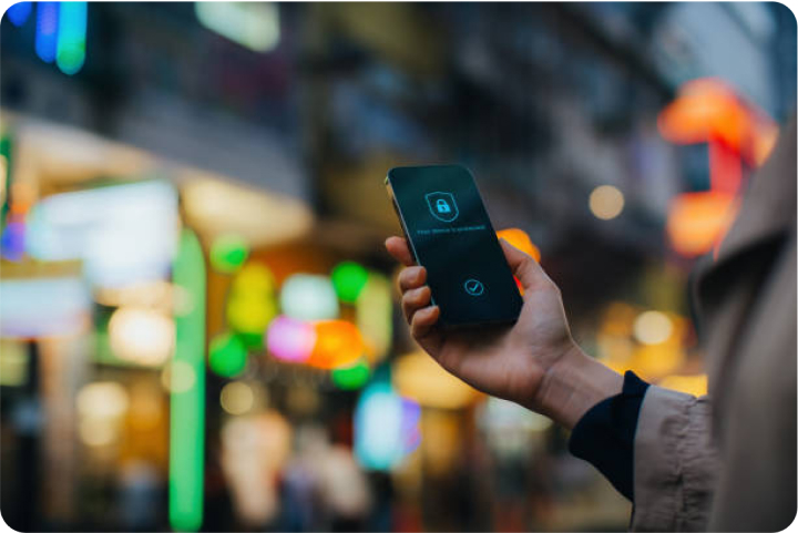 Persona que sostiene un teléfono inteligente con un ícono de candado en la pantalla, con luces borrosas de la ciudad en el fondo.